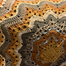 Load image into Gallery viewer, Close-up of an amber, cream, taupe, and gray crochet Superstar blanket with pale blue accents, showing granny clusters and folded star points.