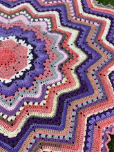 Load image into Gallery viewer, Overhead detail of a purple, pink, cream, and gray crochet Superstar blanket on grass, showing its center and radiating zigzag rows.